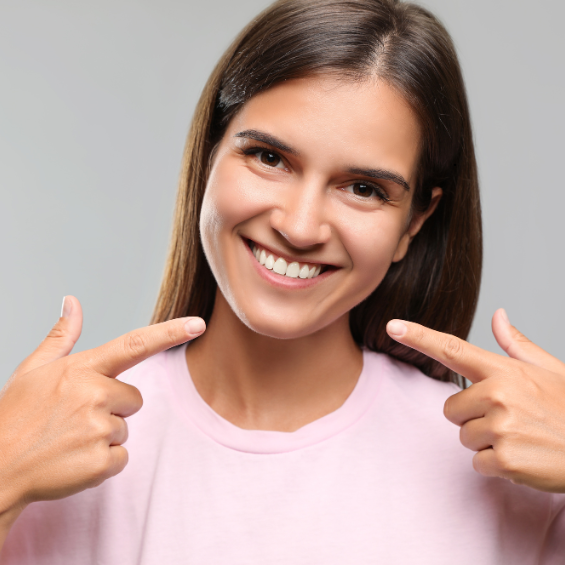 A smiling young woman points both index fingers toward her face, showcasing her teeth after a cosmetic dentistry treatment in Phoenix